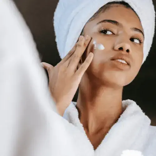 Ethnic woman applying cream on face in morning